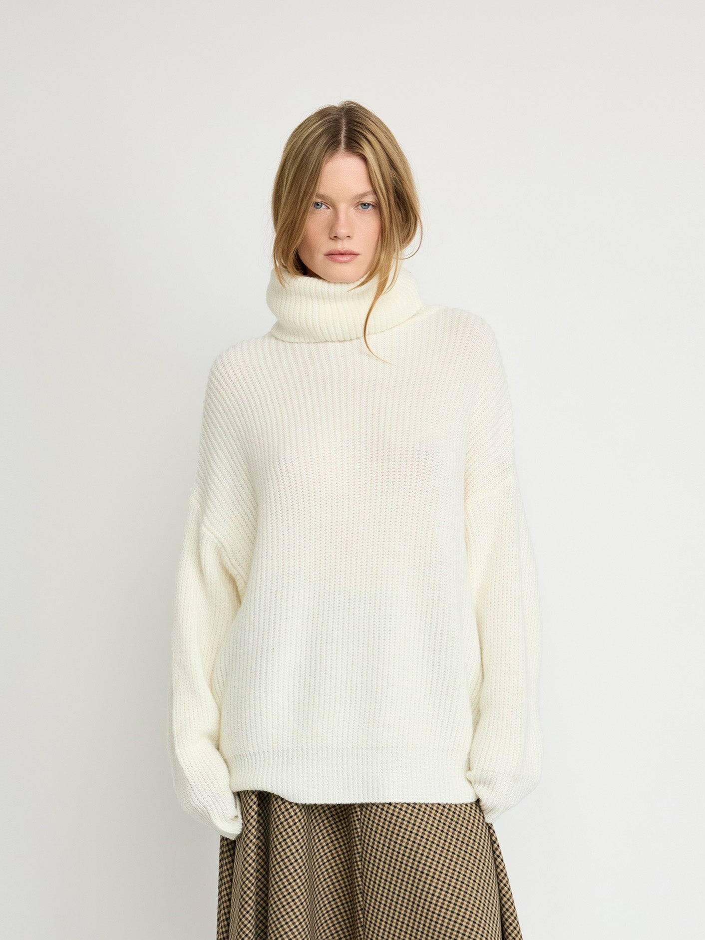 Woman wearing a white turtleneck sweater and brown checkered skirt on a white background
